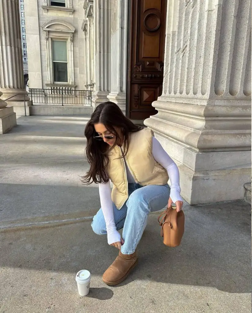 fall winter outfit wearing white bodysuit layer with beige vest pair them with mom jeans and ugg boots